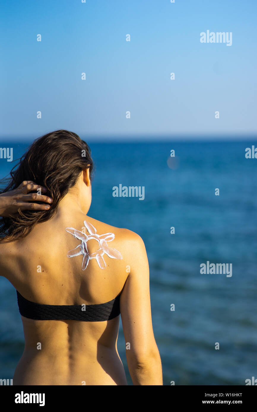 Protección de la piel - mujer joven con sun sun en forma de crema sobre su espalda al mar vista desde atrás. Foto de stock