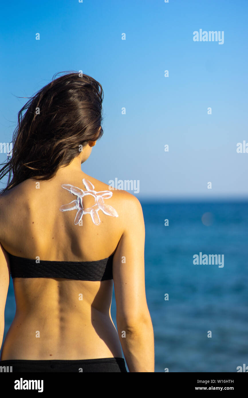 Protección de la piel - mujer joven con sun sun en forma de crema sobre su espalda al mar vista desde atrás. Foto de stock