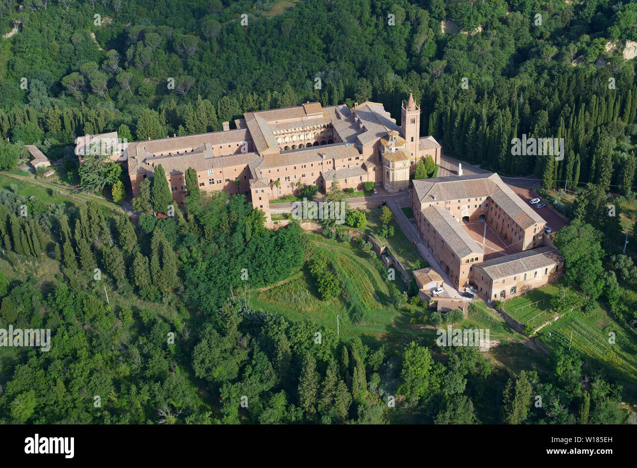 VISTA AÉREA. Abadía aislada en un entorno de colinas boscosas. Abadía de Monte Oliveto Maggiore, Asciano, Provincia de Siena, Toscana, Italia. Foto de stock