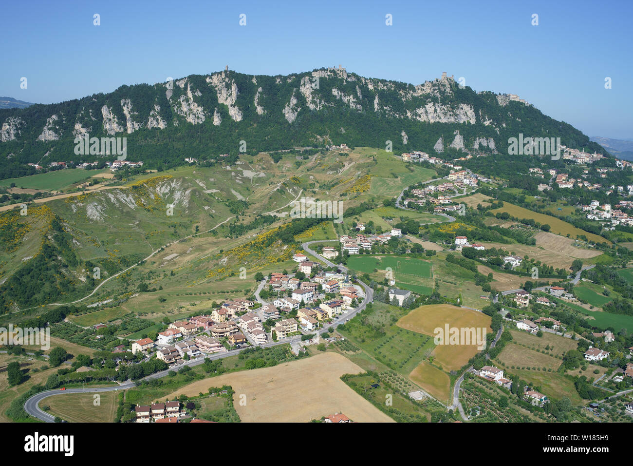 VISTA AÉREA. Monte Titano (elevación: 749m, punto más alto del país) con vistas a un paisaje de tierras de labranza y pueblos. República de San Marino. Foto de stock