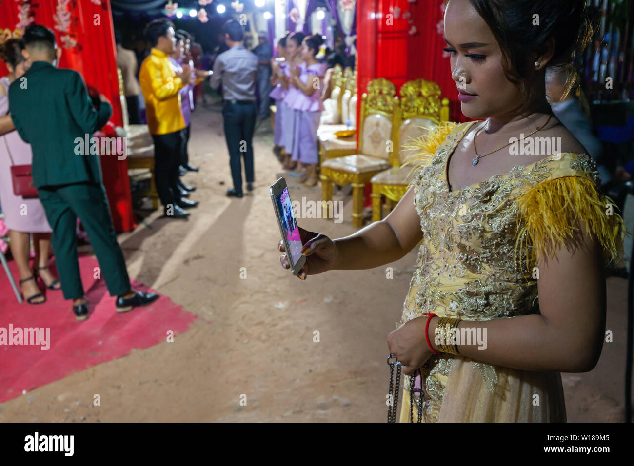 Una joven camboyana vistiendo un traje tradicional Khmer toma una fotografía con un teléfono inteligente en una boda en Siem Reap, Camboya. Foto de stock