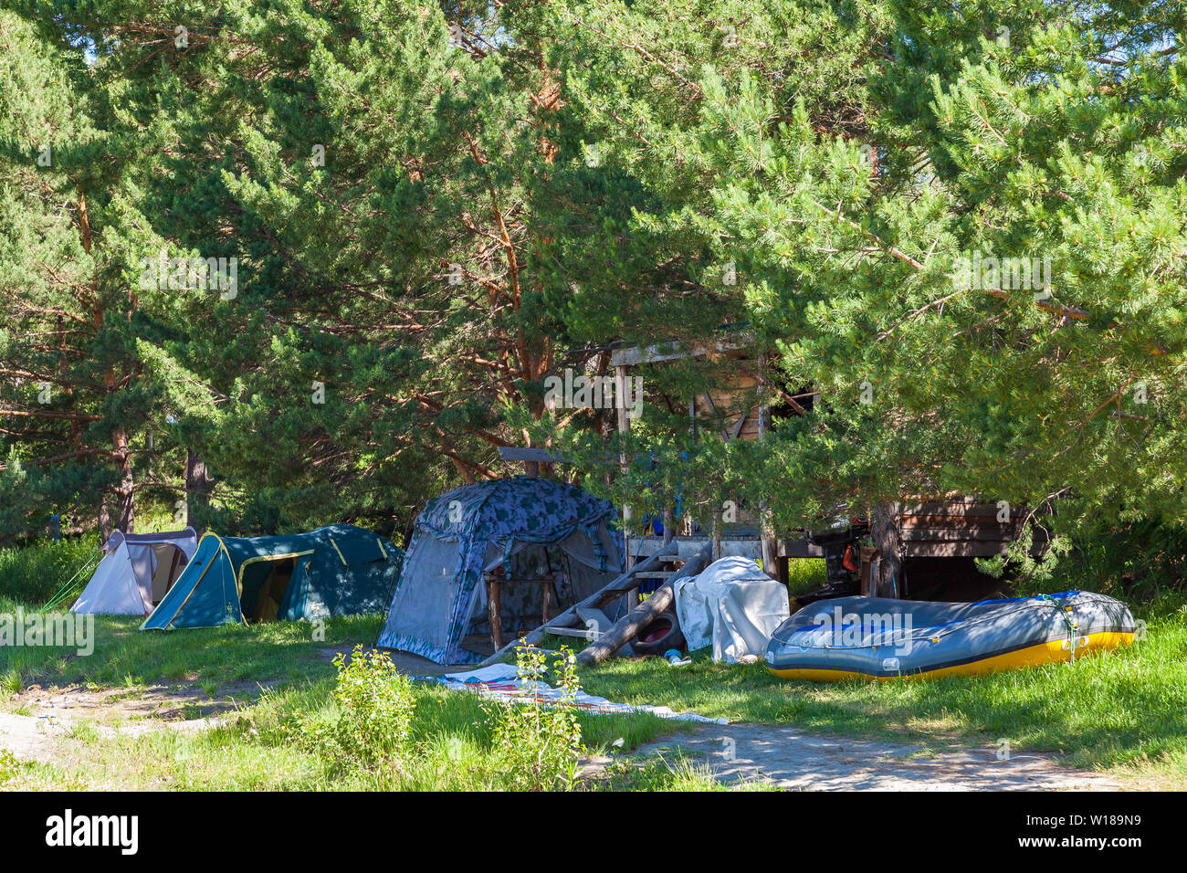 Acampar en la sombra bajo los árboles con una casa de madera y una gran  balsa inflable barco cerca del río en las montañas de Altai. Deporte  extremo Fotografía de stock -