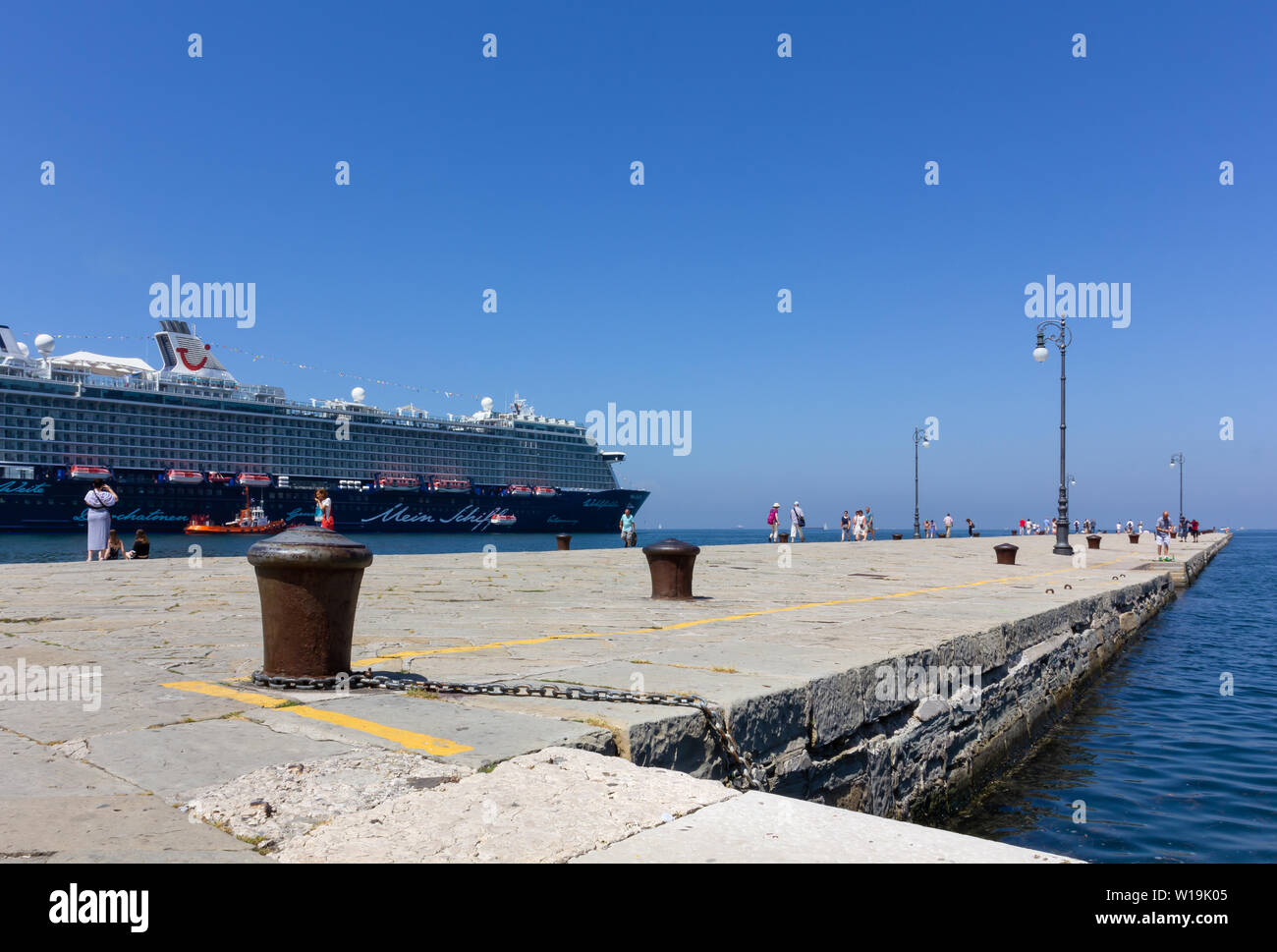 TRIESTE, Italia - 16 de junio de 2019: Los turistas paseando por el Audace pier en la ciudad de la costa y el buque de crucero Mein Schiff 6 amarrados junto a ella Foto de stock