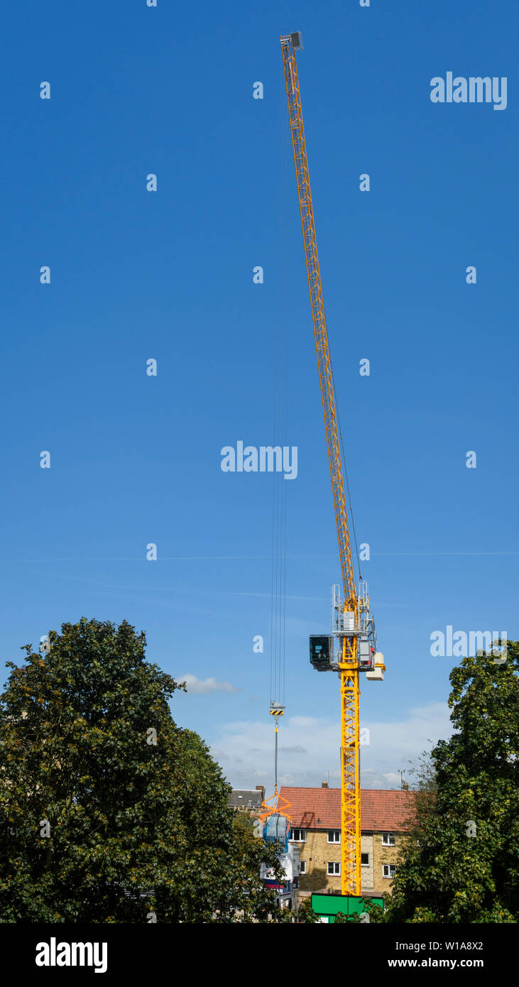 Tall amarillo grúa torre de elevación y trabajando en la construcción sitio contra el cielo azul profundo (Cabina del operador, MAST y pescante) - York, North Yorkshire, Inglaterra, Reino Unido. Foto de stock