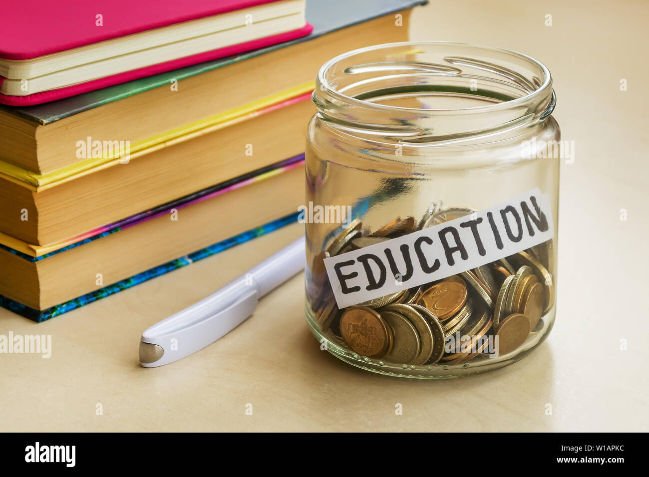 Frasco de vidrio con un montón de monedas y educación palabra cerca de white bolígrafo y algunos libros sobre una mesa. Ahorro de dinero por concepto de educación. La planificación. Foto de stock