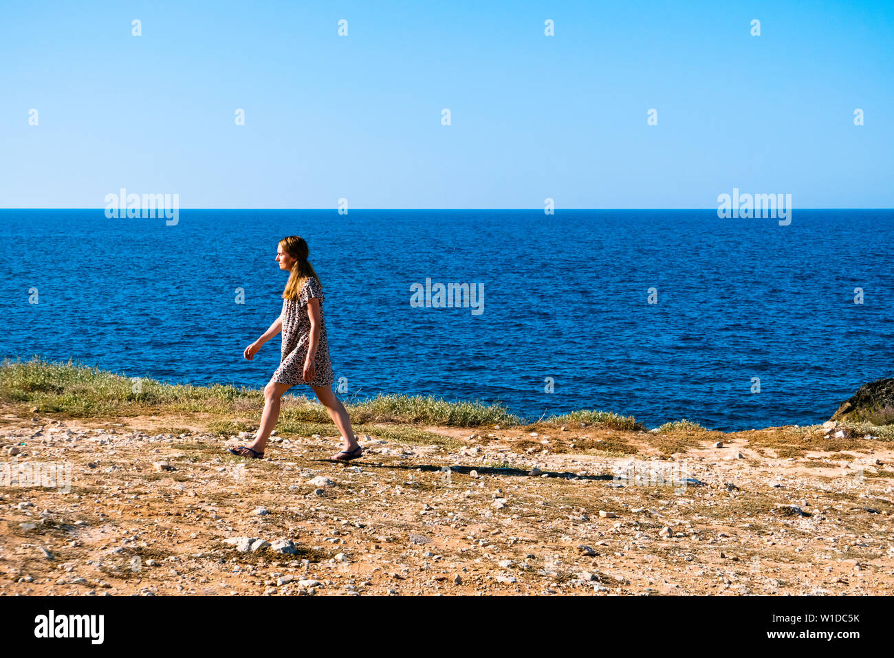 Polignano,Italia ; una mujer vestida como hipster en la costa adriática de Polignano en un atardecer de verano solo que camina en dirección al sol. Foto de stock