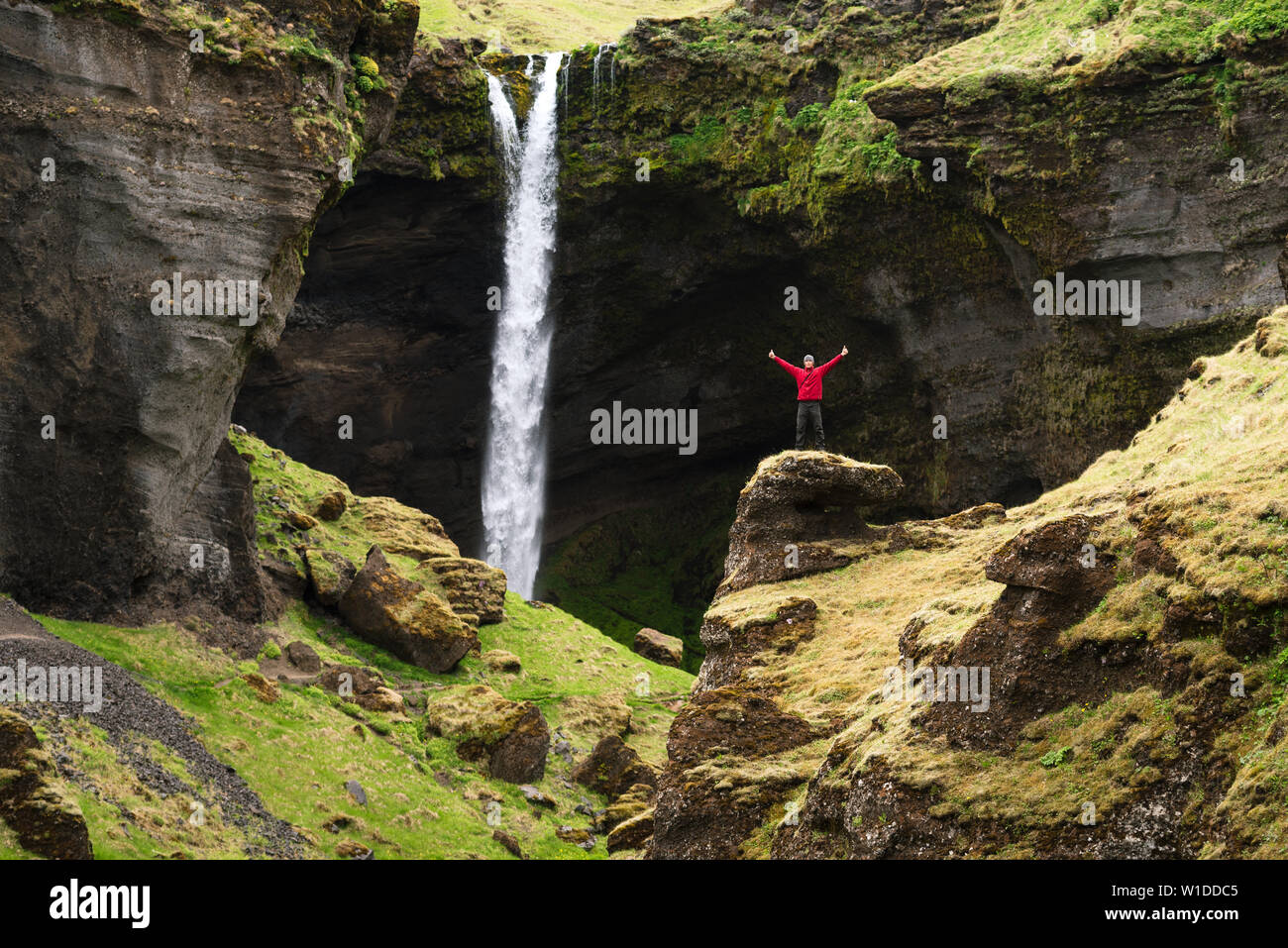 Kvernufoss cascada en Islandia. El Turista en una chaqueta roja inspecciona la vista Foto de stock