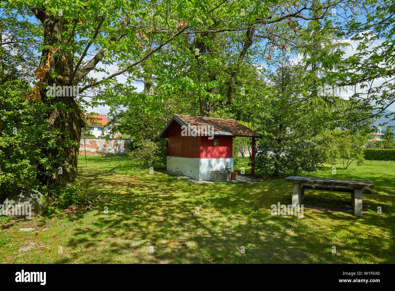 Jardín, pequeña casa roja y mesa de piedra en un día soleado de verano, Italia Foto de stock