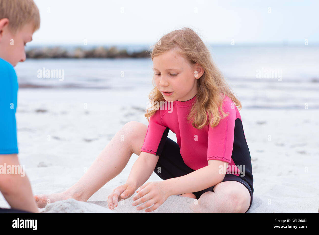 Irradiar regimiento muerte Dos niños felices en trajes de baño de neopreno jugando en la playa con  arena Fotografía de stock - Alamy