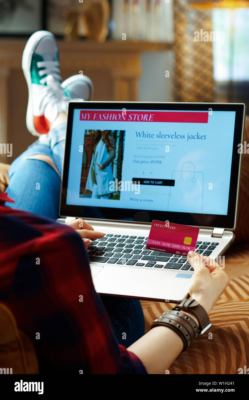 Sobre el hombro shot de la moda hipster en rojo camisa a cuadros, jeans y  zapatillas de color rosa con tarjeta de crédito comprar ropa mientras  tienda online mientras está sentado o