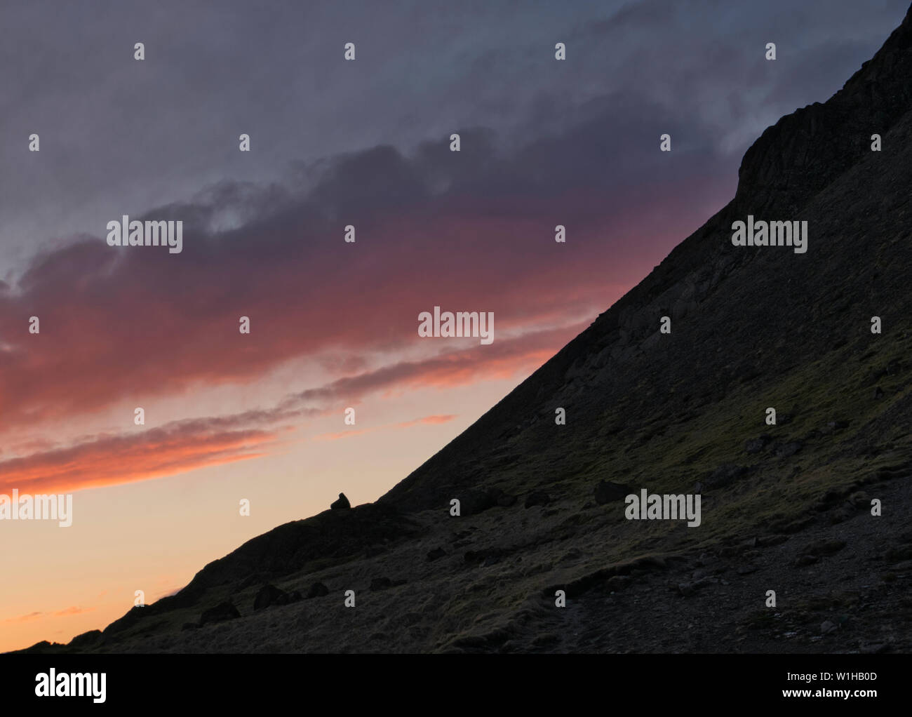 Una empinada ladera de montaña en Islandia al atardecer con las nubes de colores Foto de stock