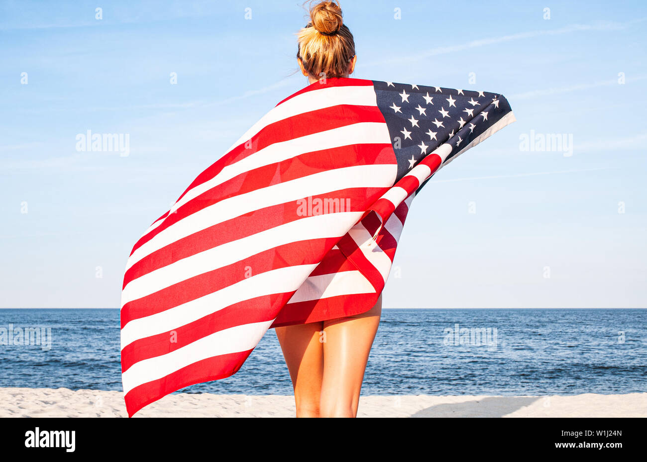 Hermosa mujer patriótica con bandera americana en la playa. Día de la Independencia de EE.UU., 4 de julio. Concepto de libertad, vista desde la parte de atrás. Foto de stock