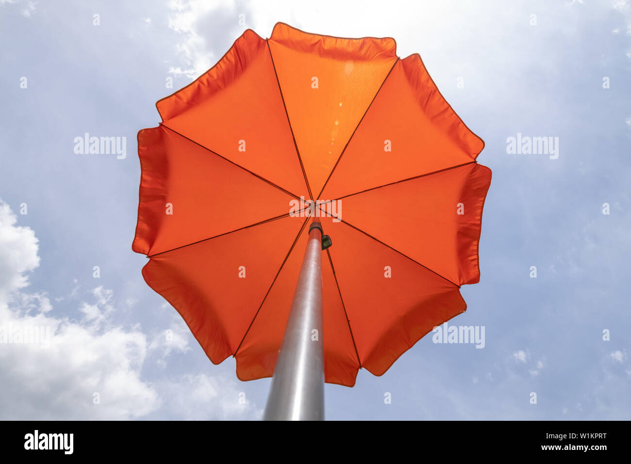 Foto de una sombrilla en el cielo azul,playa sombrilla.un vibrante color naranja sombrilla contra un intenso azul cielo y nube blanca. Foto de stock
