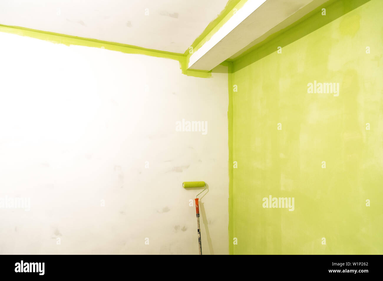 Rodillo para pintar cerca de una pared pintada de verde Foto de stock