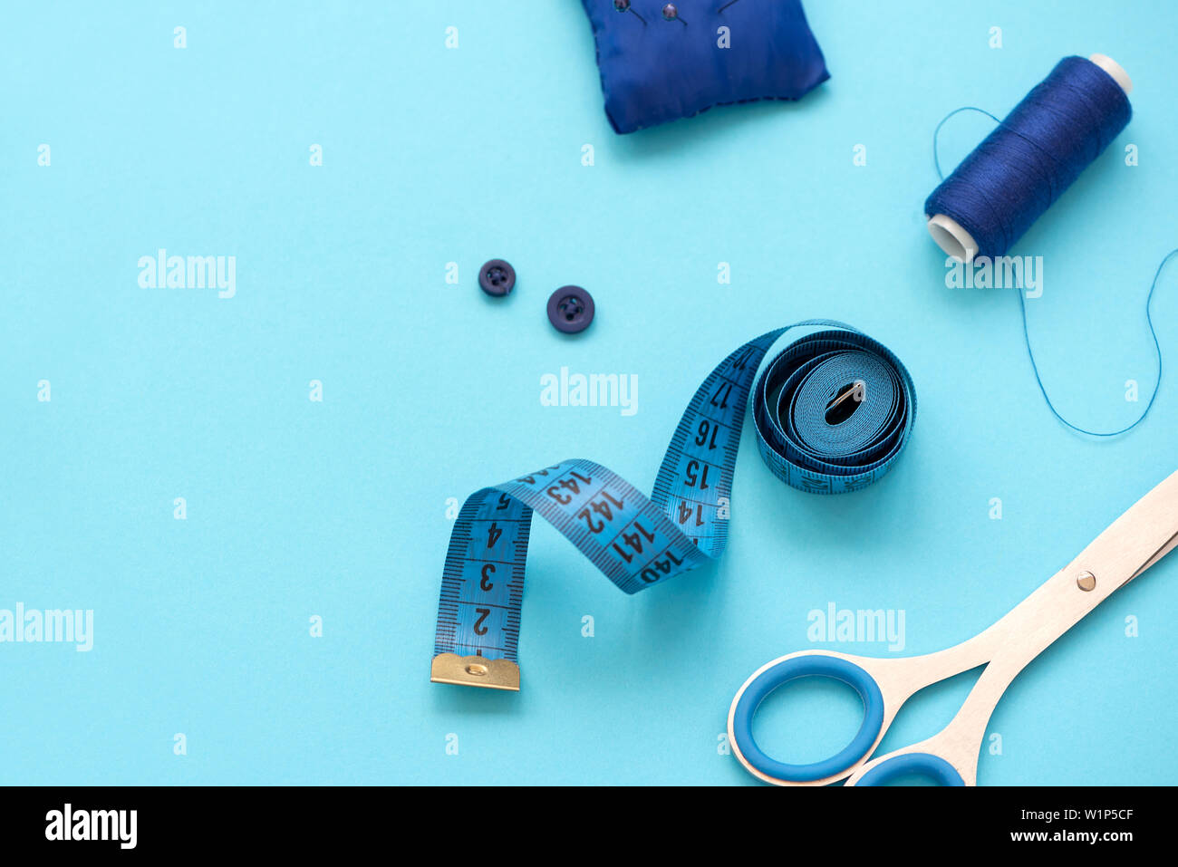 Accesorios de costura con hilos, tijeras, alfileres, tela, botones y cintas de coser sobre fondo azul. Vista desde arriba. Sentar planas. Foto de stock