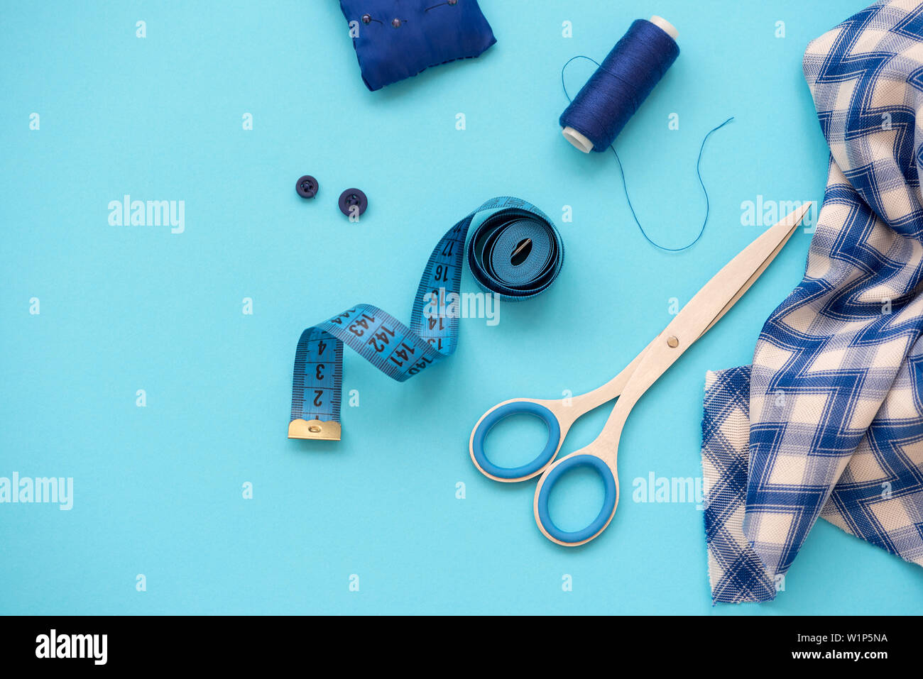 Accesorios de costura con hilos, tijeras, alfileres, tela, botones y cintas de coser sobre fondo azul. Vista desde arriba. Sentar planas. Foto de stock