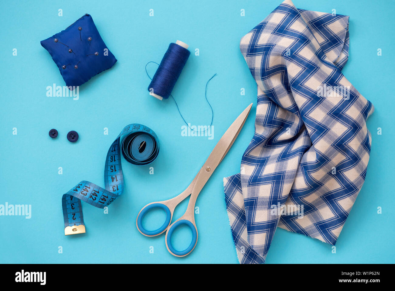 Accesorios de costura con hilos, tijeras, alfileres, tela, botones y cintas de coser sobre fondo azul. Vista desde arriba. Sentar planas. Foto de stock