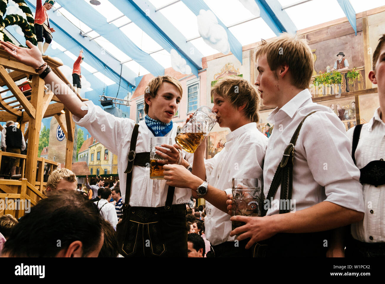 Los hombres jóvenes en pantalones de cuero de pie sobre la cerveza bancos celebrar la Oktoberfest en la tienda de cerveza Foto de stock