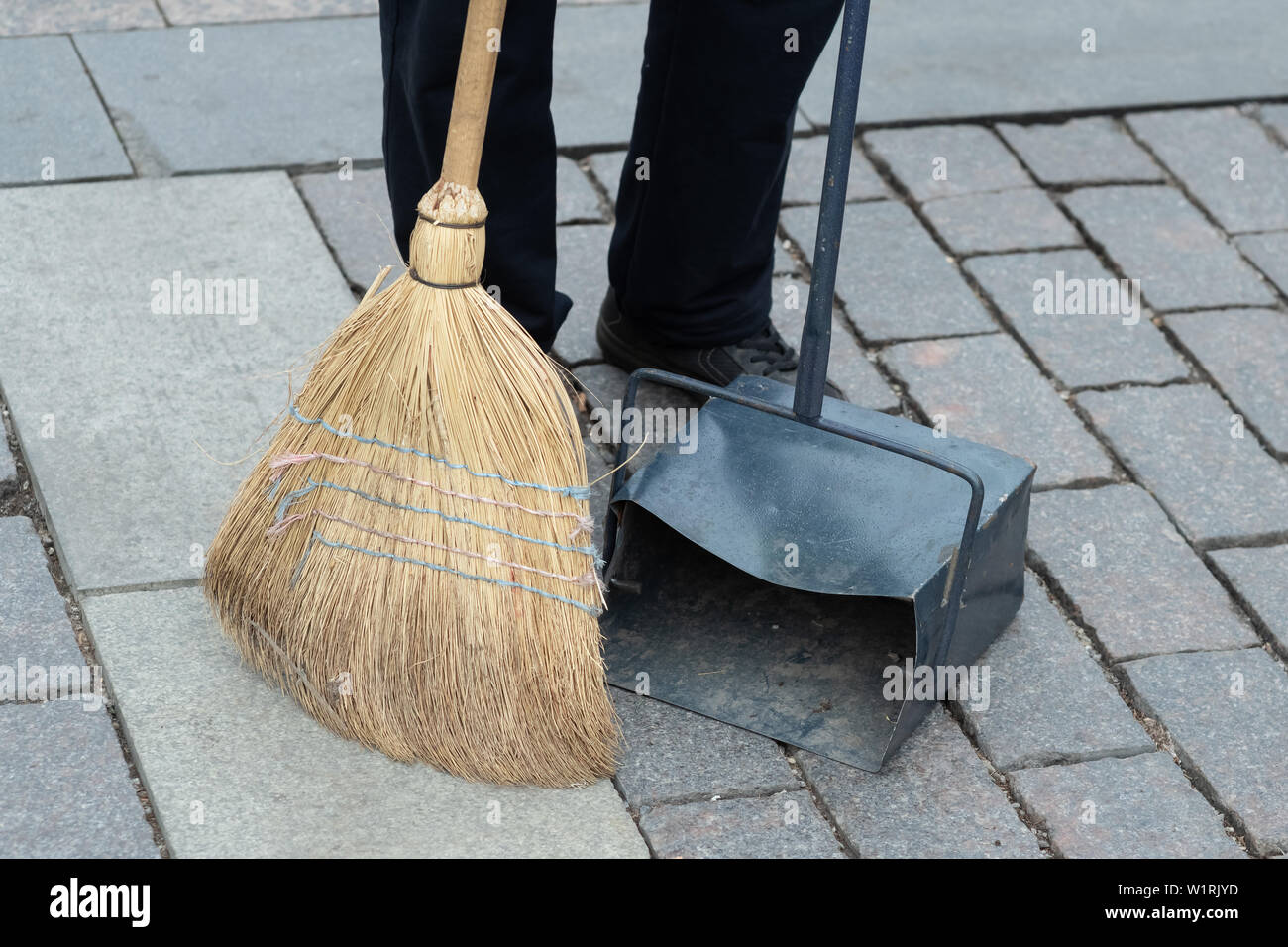 Descripción: trabajador municipal barren la carretera con la escoba y recoge la basura en boca. saneamiento calle barrido trabajador Foto de stock
