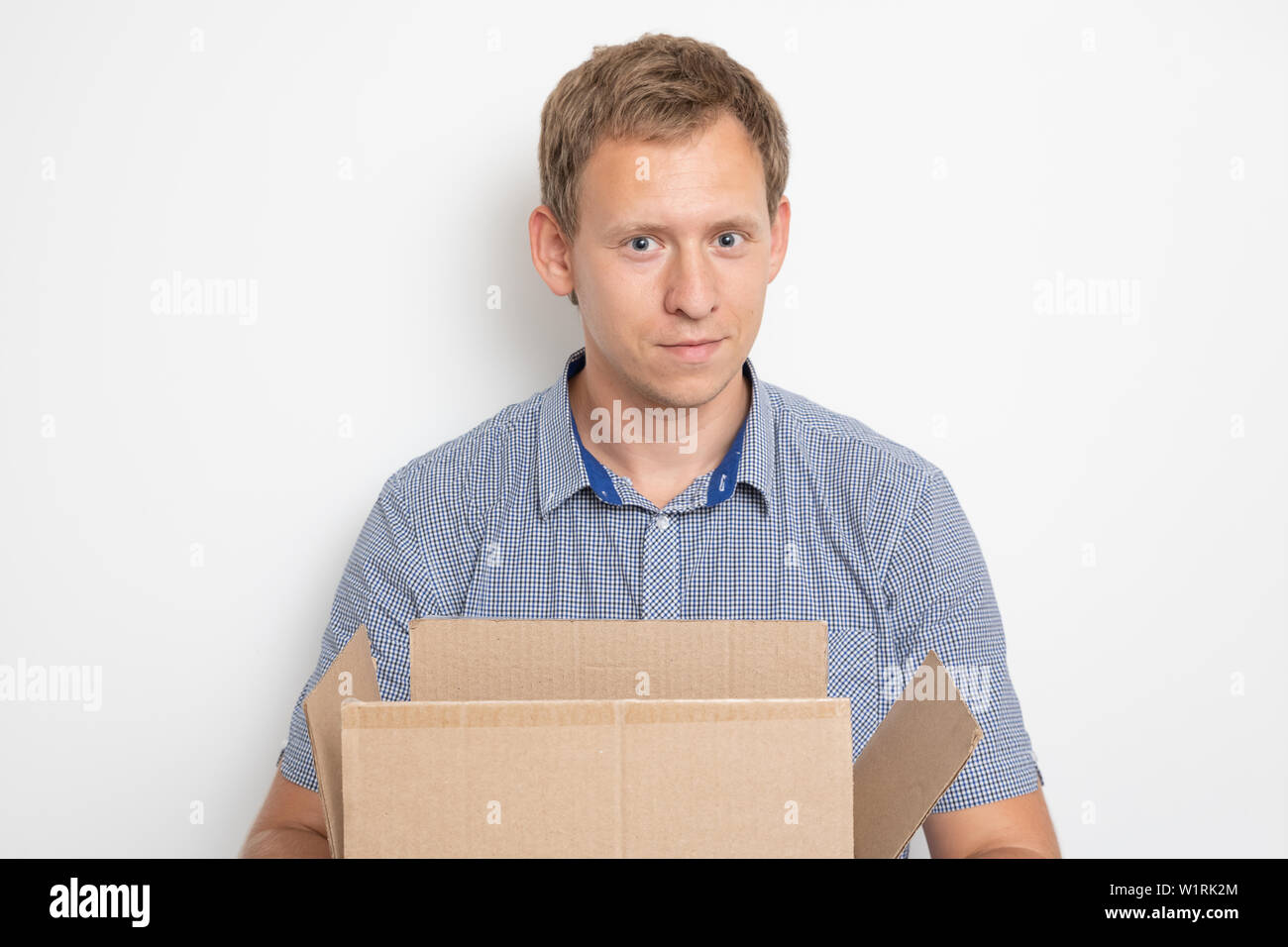 Descripción: un joven apuesto hombre caucásico mantiene abierta una caja de cartón en sus manos y sonrió Foto de stock