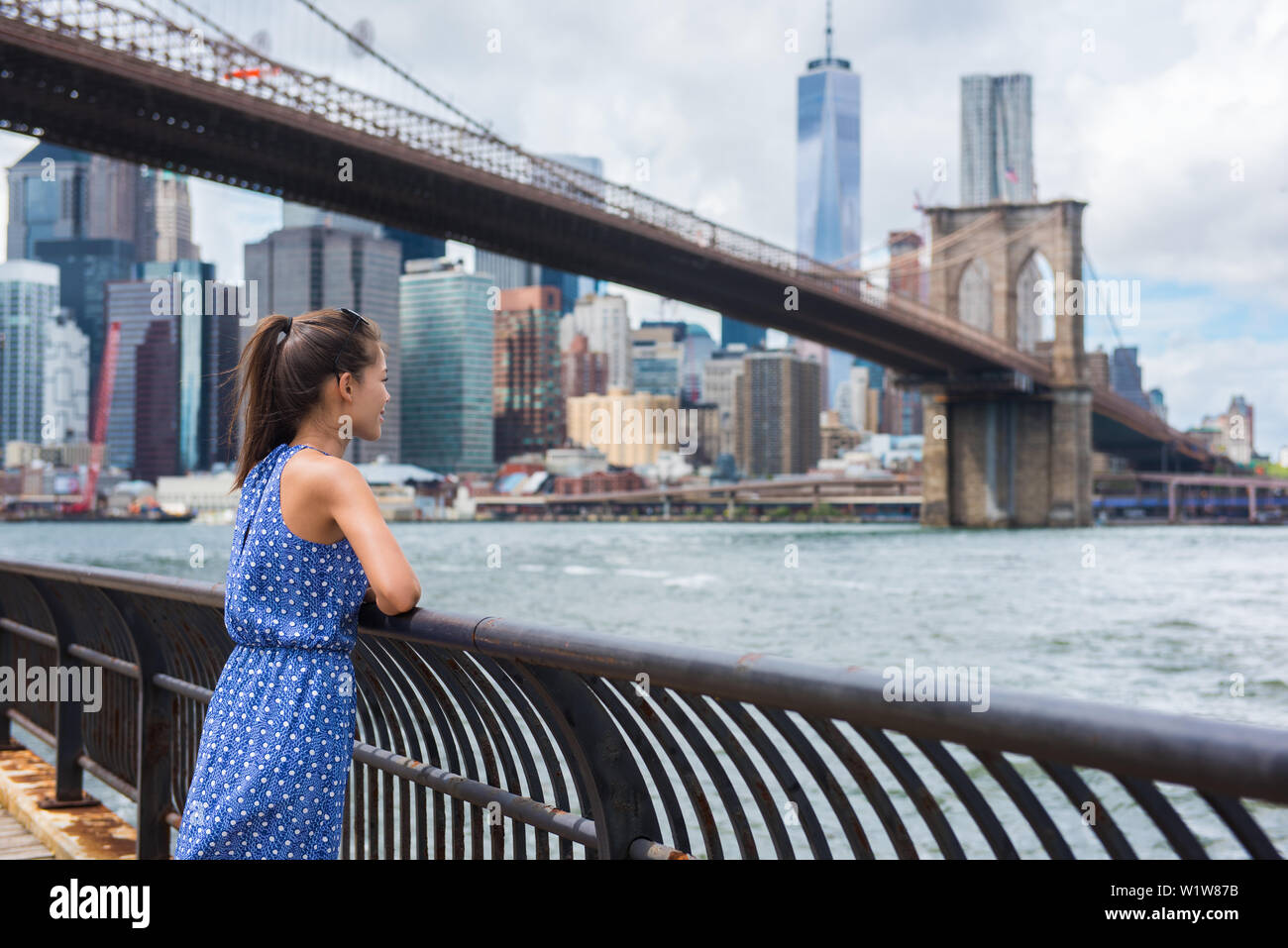 Mujer urbana de la ciudad de Nueva York disfrutando de vistas del puente de Brooklyn y NYC skyline viviendo una vida feliz caminar durante el viaje de verano en EE.UU. Turismo Asiático Femenino en su 20s. Foto de stock