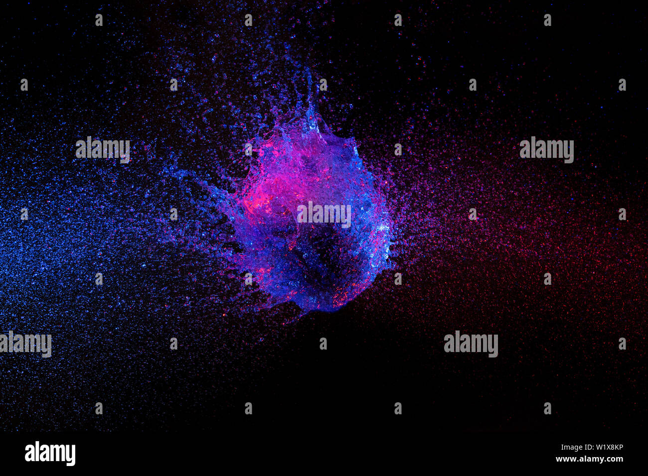 La fotografía de alta velocidad. El globo lleno de agua fotografiado en el instante exacto del impacto y romper. azul y púrpura, luces de fondo negro. Foto de stock