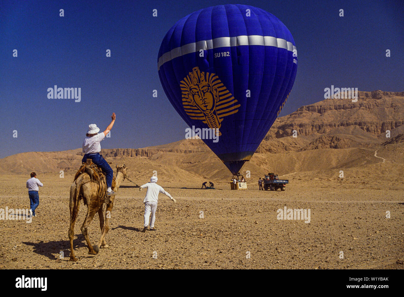 En globo de aire caliente sobre el valle de los Reyes, Luxor, Egipto. Un turista sigue el globo en el camelback. Foto: © Simon Grosset. Archivo: Imagen digi. Foto de stock