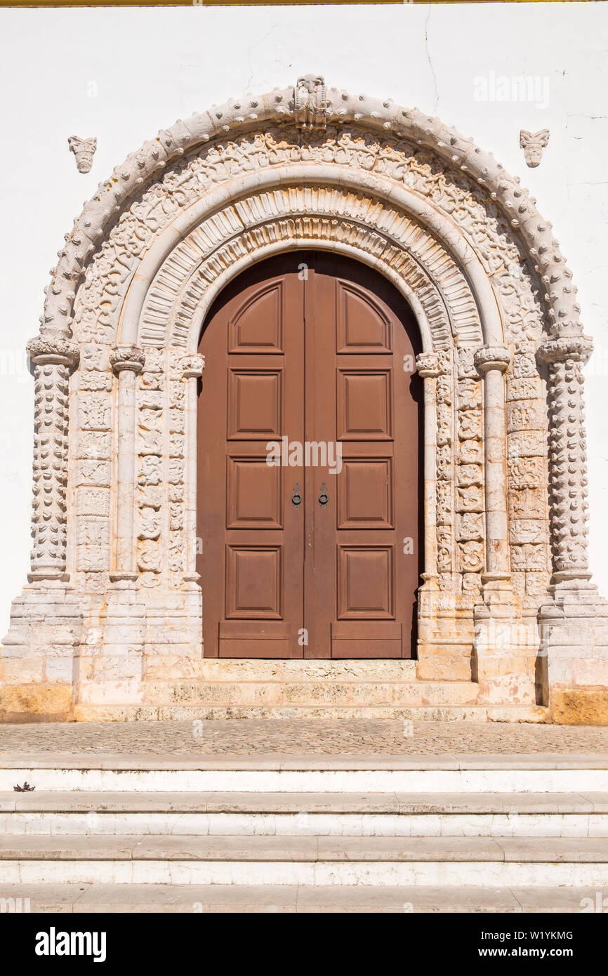Las grandes puertas de la iglesia de madera con ornamentación en piedra alrededor de ellos en Alvor, Algarve, Portugal Foto de stock