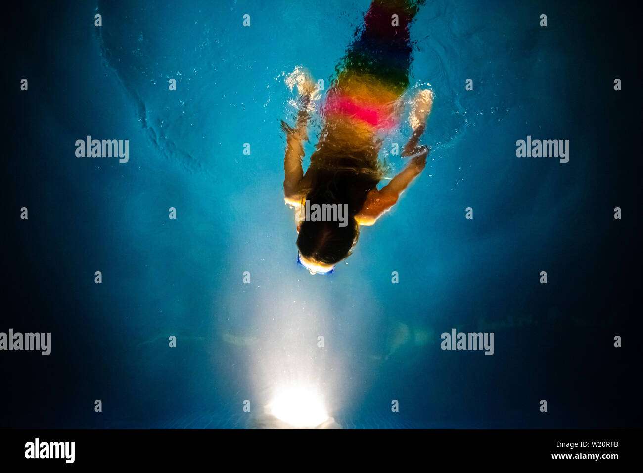Buceo de sirena hacia la luz de una piscina azul en la noche, con un fondo de ensueño de la fantasía y la imaginación. Foto de stock