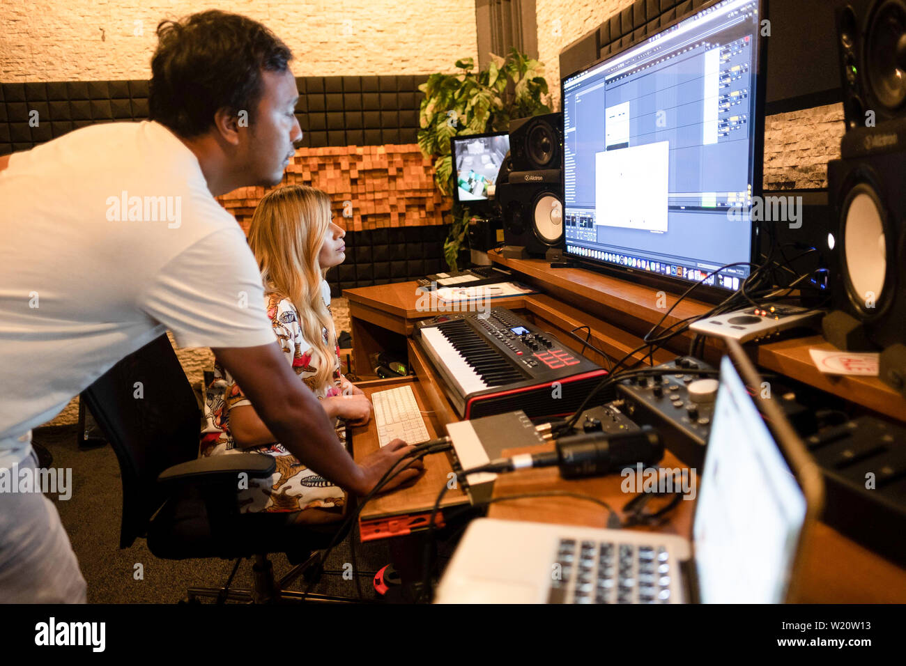 El ingeniero de sonido produciendo con una rubia mujer músico en un moderno estudio de música Foto de stock
