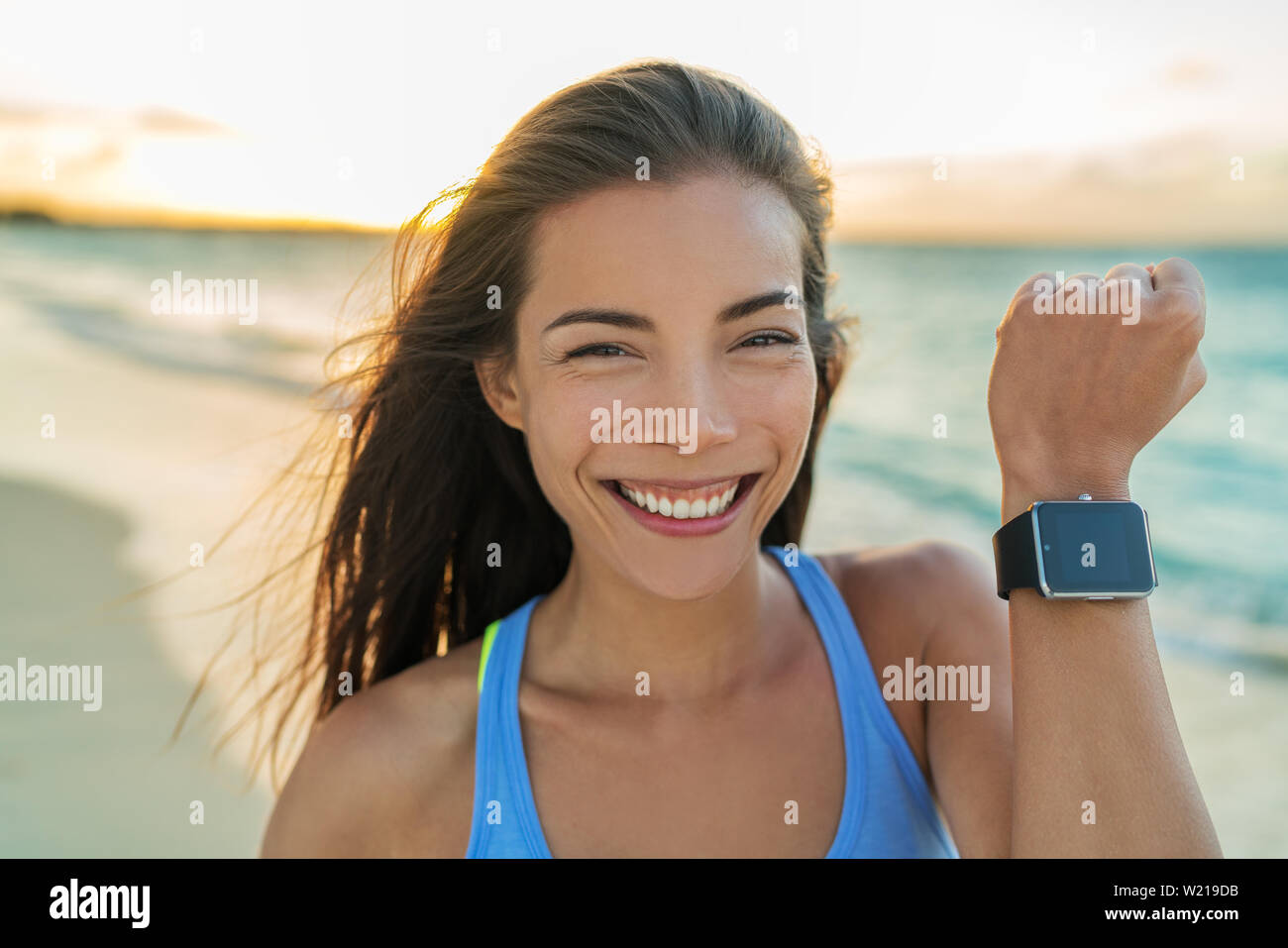 Smartwatch niña alegre que muestra la pantalla de moderno y nuevo reloj inteligente fitness tracker reloj de pulsera. Jóvenes sanos deportiva asiática mujer sonriente en la playa de vacaciones girando al atardecer que viven una vida activa. Foto de stock