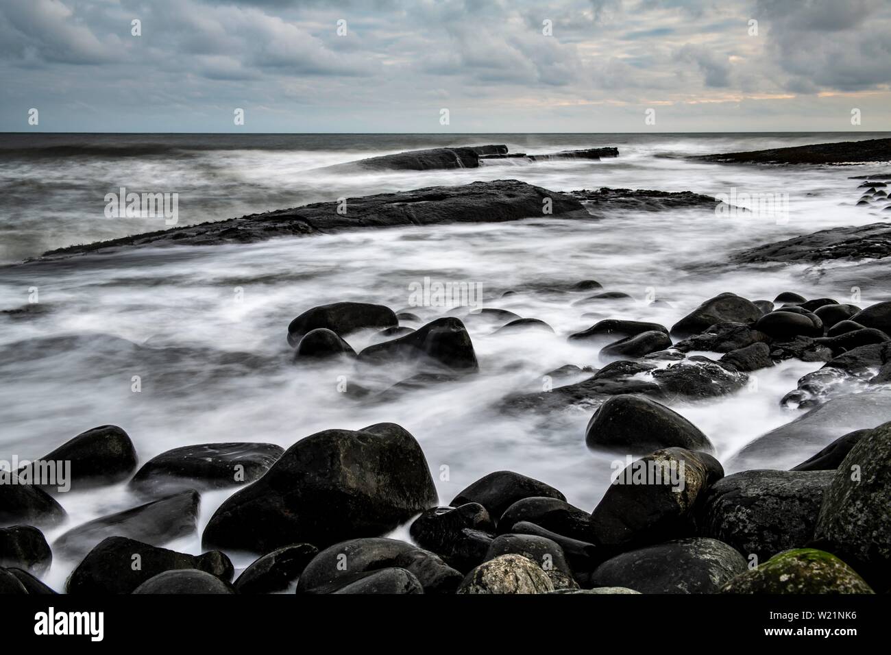 Negro, piedras redondas en el surf, Craster, Northumberland, Gran Bretaña Foto de stock