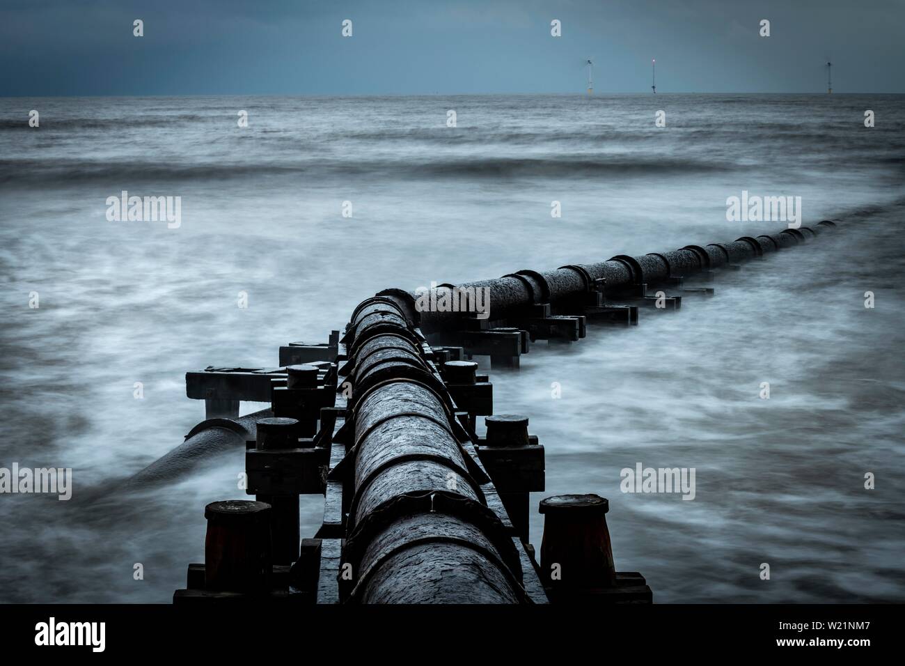 Tubo de hierro oxidadas, tubo de aguas residuales en el mar navegar bajo un cielo oscuro, Blyth, Northumberland, Gran Bretaña Foto de stock