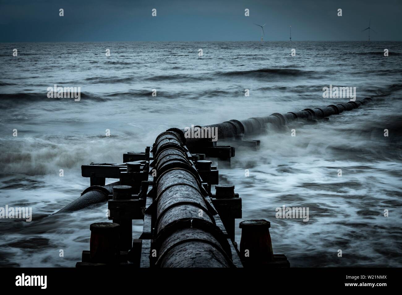 Tubo de hierro oxidadas, tubo de aguas residuales en el mar navegar bajo un cielo oscuro, Blyth, Northumberland, Gran Bretaña Foto de stock