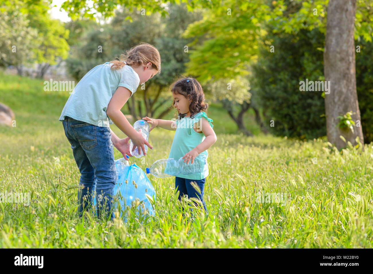 Contaminación plástica en tierra. Cildren recogiendo una botella plástica de hierba en el Parque contaminado. Foto de stock