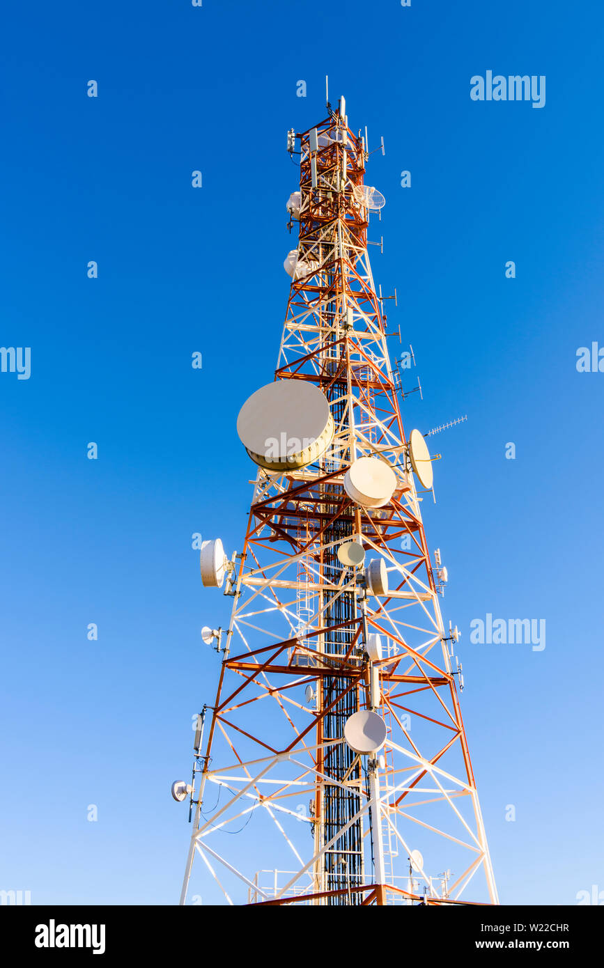 Gran mástil de telecomunicaciones en la cima de una montaña pintada de rojo y blanco, y contiene muchos platos de microondas, teléfonos móviles, antenas dipolos yagis Foto de stock