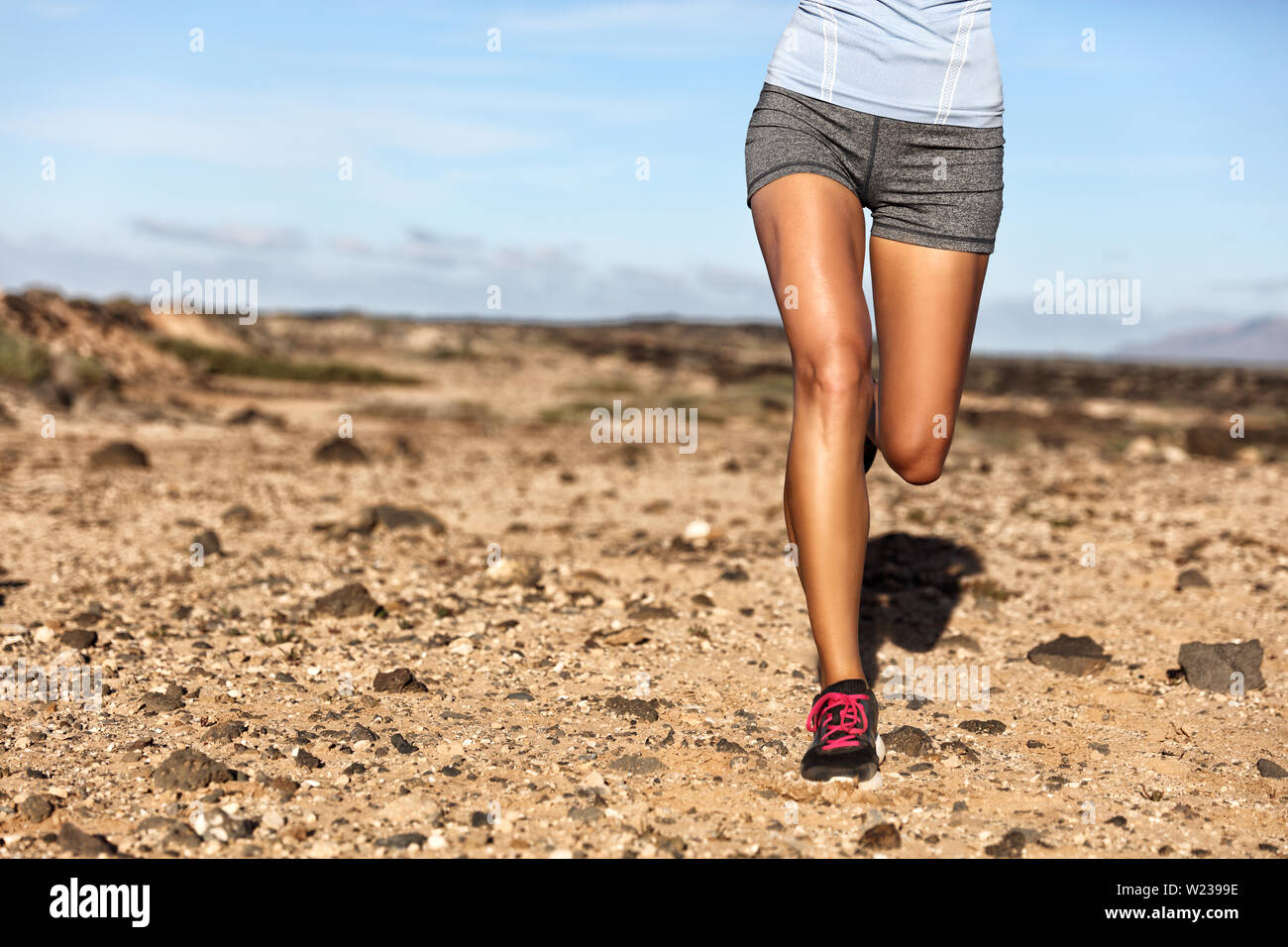 Verano atleta trail runner piernas cuerpo inferior de cosecha. Mujer Fitness trotar viviendo un estilo de vida activo trotar en camino rocoso en la naturaleza del paisaje de montaña. Zapatos, rodillas, muslos, concepto de pérdida de peso. Foto de stock
