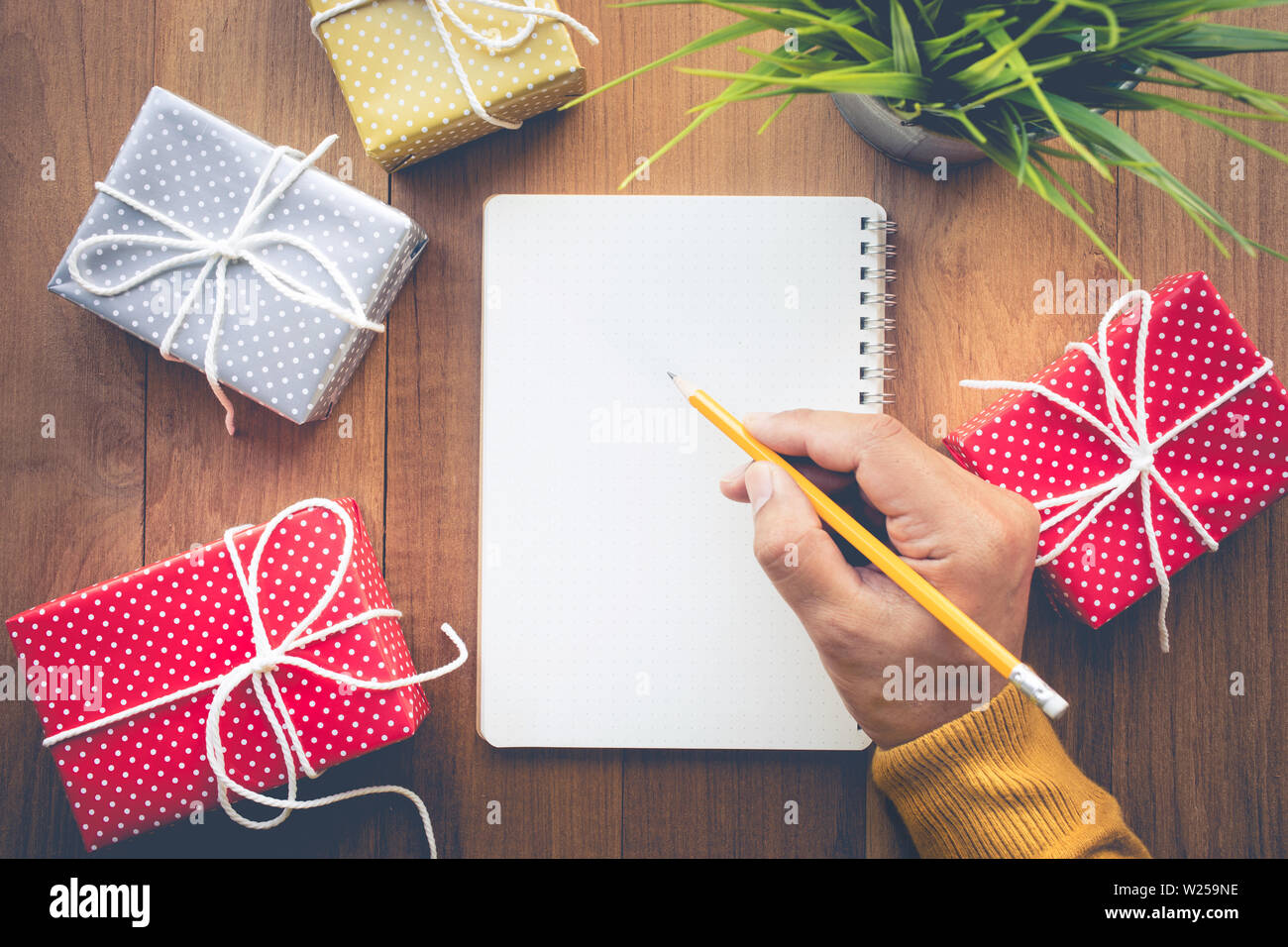 Hombre mano escribiendo una nota de papel con lindos regalos en caja de regalo de fondo la tabla de trabajo.Para navidad, año nuevo, cumpleaños y felicidad conceptos ideas Fotografía de stock -