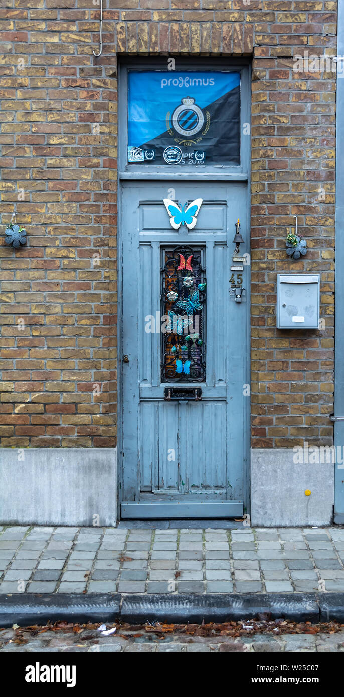 Brujas, Bélgica - 16 de diciembre de 2018: azul antiguo soportó la puerta en una pared de ladrillo. Vintage delantera azul decorado con mariposas. Foto de stock