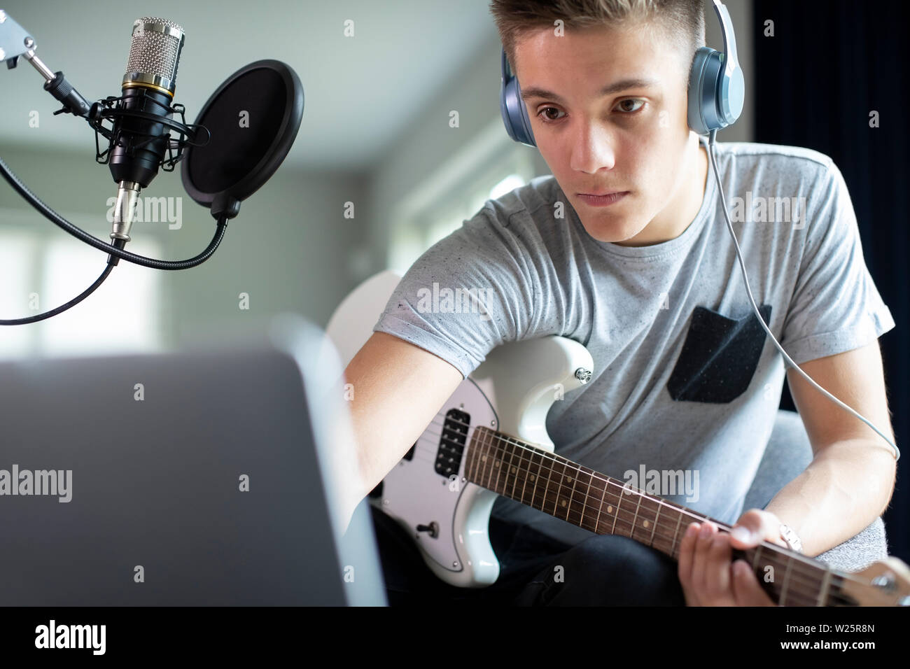 Adolescente tocando la guitarra y la grabación de música en el ordenador portátil en casa Foto de stock