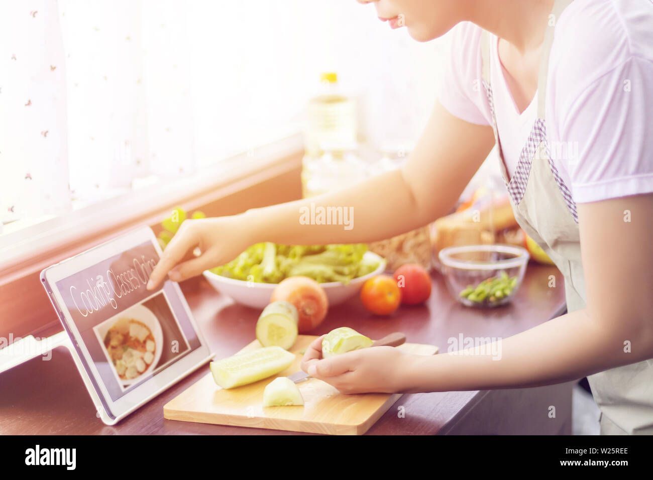 Mujer Asiática preparar los ingredientes para cocinar siga cooking class curso en línea en el sitio web a través de la tableta. Cocinar el contenido de la tecnología de internet para moder Foto de stock