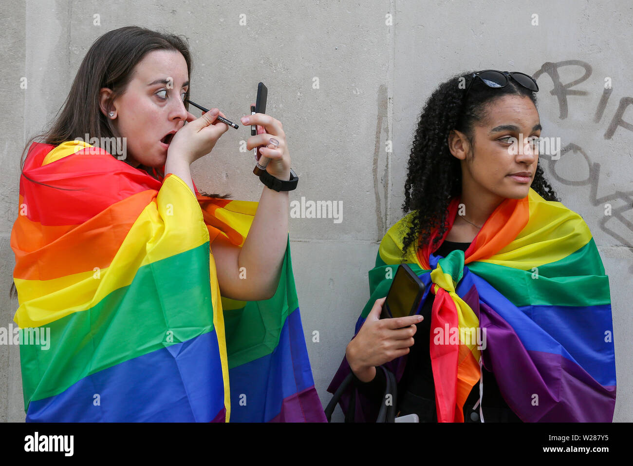 Dos juerguistas con banderas del arco iris ponerme maquillaje durante el   mayor orgullo en Londres desfile en el centro de Londres. Un  estimado de más de 1 millones de personas alineadas