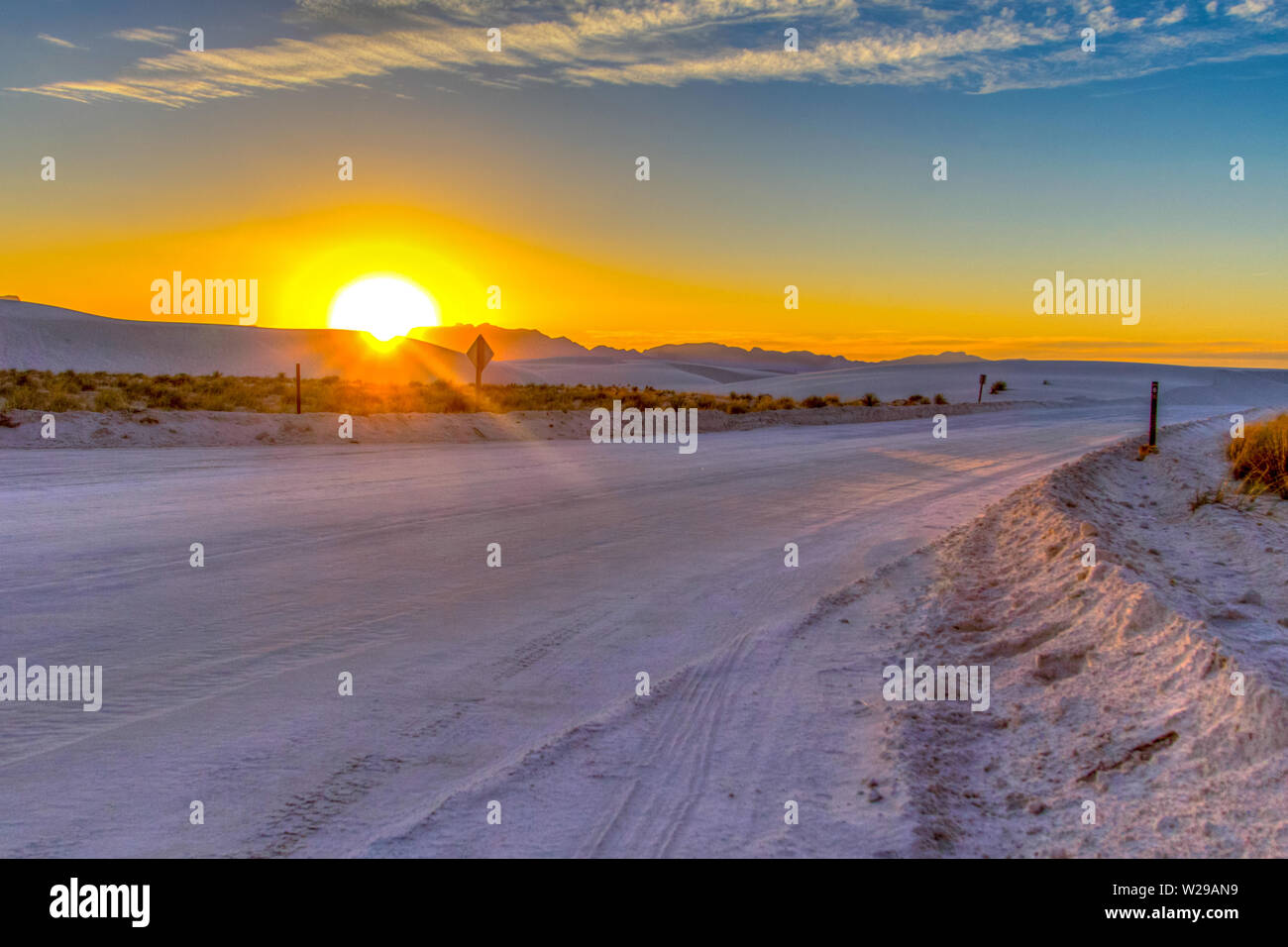 Ruta Por El Desierto. Hermosa puesta de sol en el desierto con un camino rural remoto serpenteando por las dunas de arena del Monumento Nacional White Sands en Nuevo México. Foto de stock