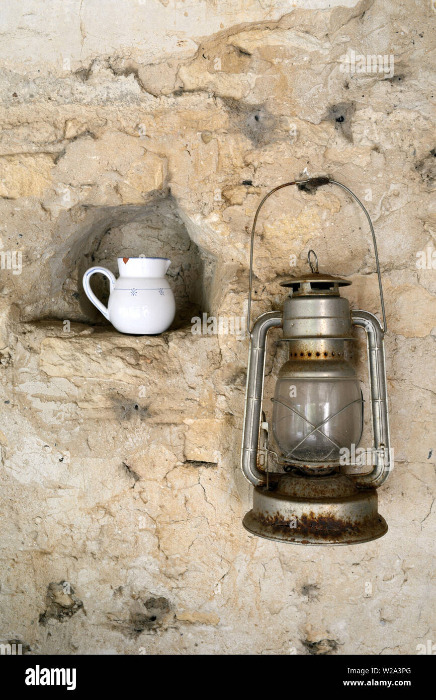 Antiguo o Vintage lámpara de aceite colgada en la pared de la jarra de leche y en nichos de Still Life contra el antiguo muro de piedra Foto de stock