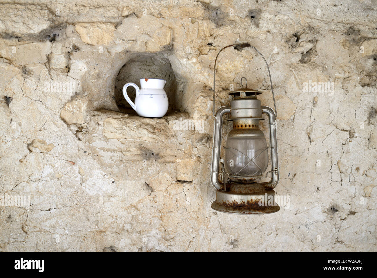 Antiguo o Vintage lámpara de aceite colgada en la pared de la jarra de leche y en nichos de Still Life contra el antiguo muro de piedra Foto de stock