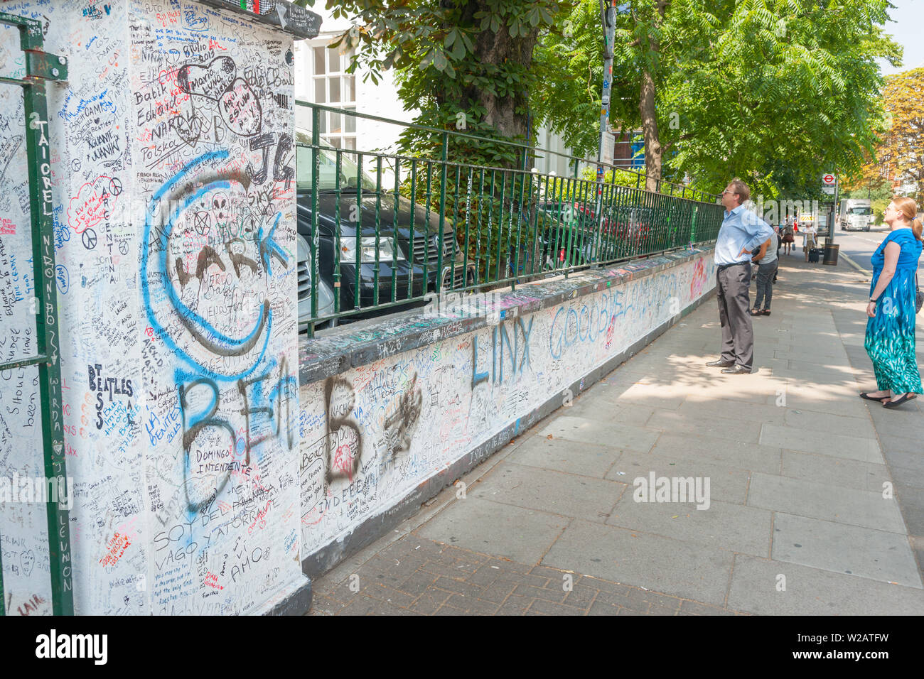 Londres - Inglaterra _ 17 de julio de 2013; la pareja de turistas en Abbey Road fuera Famous Studios mirando por encima del muro cubierto de graffiti. Foto de stock