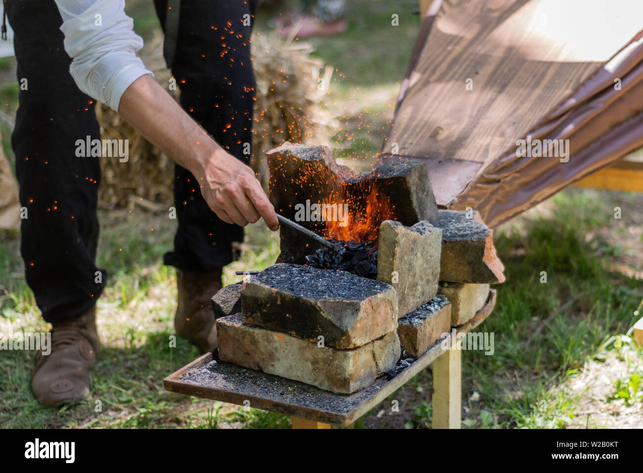 Mano con un pedazo de hierro se calienta en un fuego de carbón y fuelles  hacer chispas con las herramientas de herrero. El proceso de fabricación de  herramientas de metal y arma