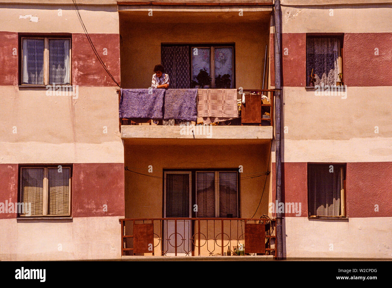 Bucarest, Rumania. De mayo de 1990. Una mujer mira hacia abajo desde el balcón en un bloque de apartamentos. Foto: © Simon Grosset. Archivo: Imagen digitalizada de una transparencia original. Foto de stock