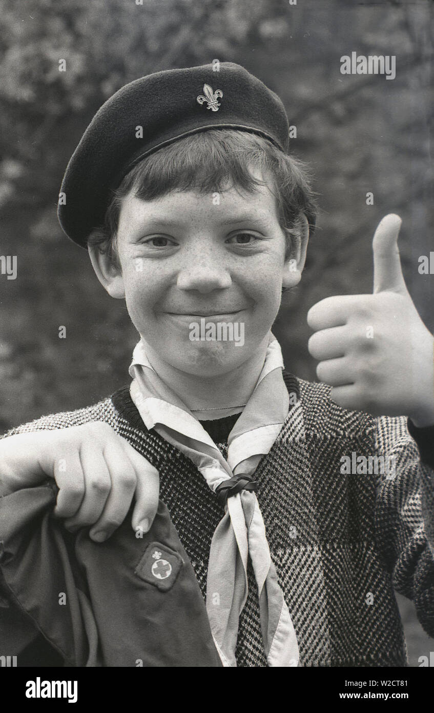 1980, histórico, joven adolescente boy scout vistiendo una boina y bufanda  y manteniendo su chaqueta con una insignia scout embrodied, dando el Thumbs  up! Fotografía de stock - Alamy