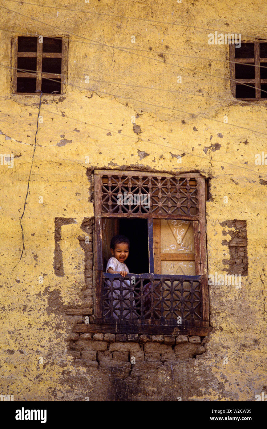 Luxor, Egipto. Un niño mirando por la ventana. Edificio antiguo, la decadencia de la pared, balcón de madera. Foto: © Simon Grosset. Archivo: Imagen digitalizada de una transparencia original. Foto de stock